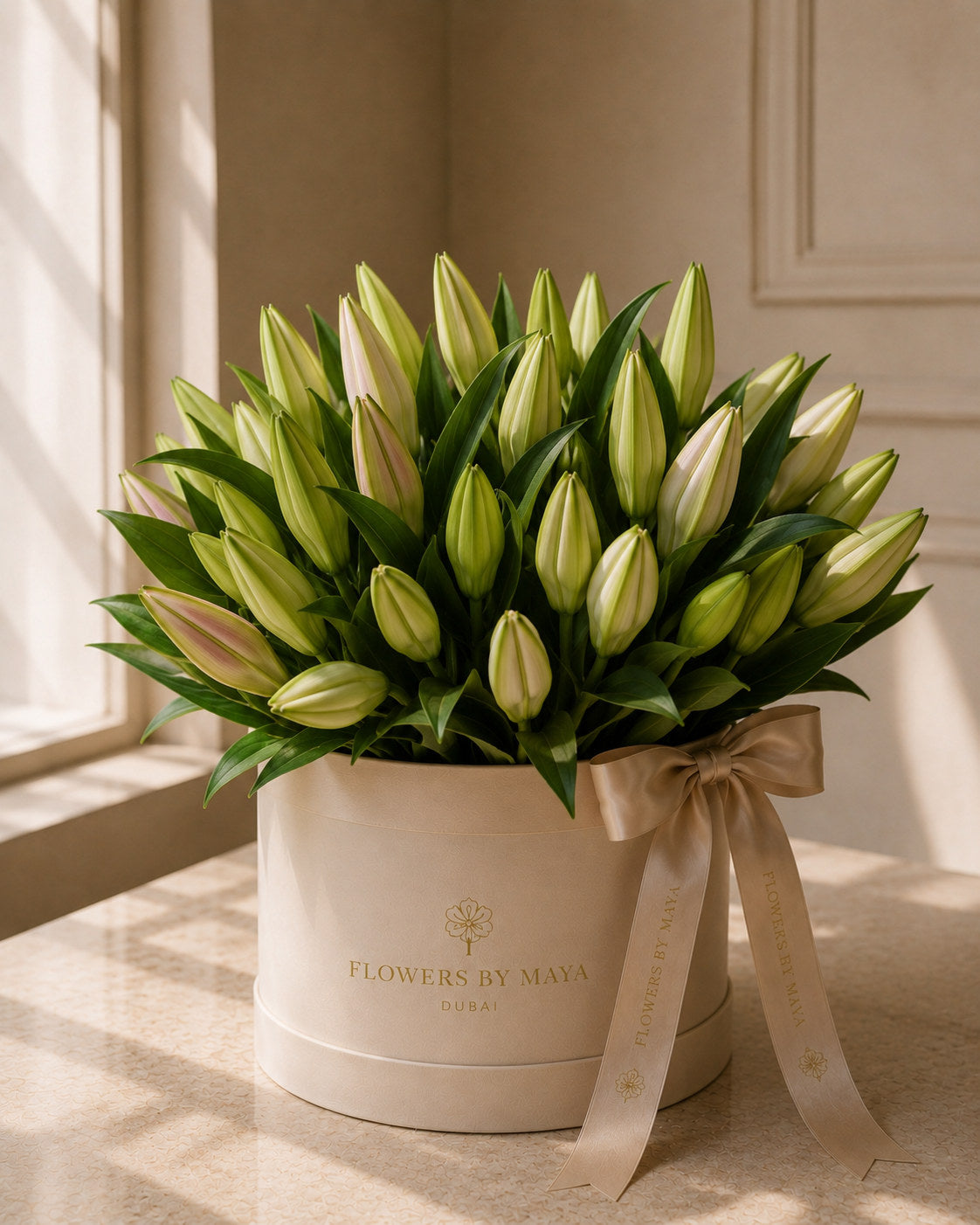 White Lily Hat Box by Flowers By Maya, white oriental lily buds with green foliage in a cream suede hat box