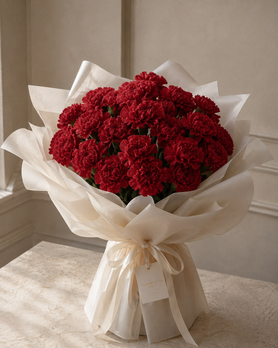 Red Carnation Bouquet by Flowers By Maya, deep crimson carnations in layered ivory tissue wrap with satin bow
